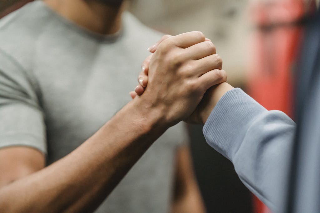 Close-up of a handshake between two individuals in a gym, symbolizing support and teamwork.